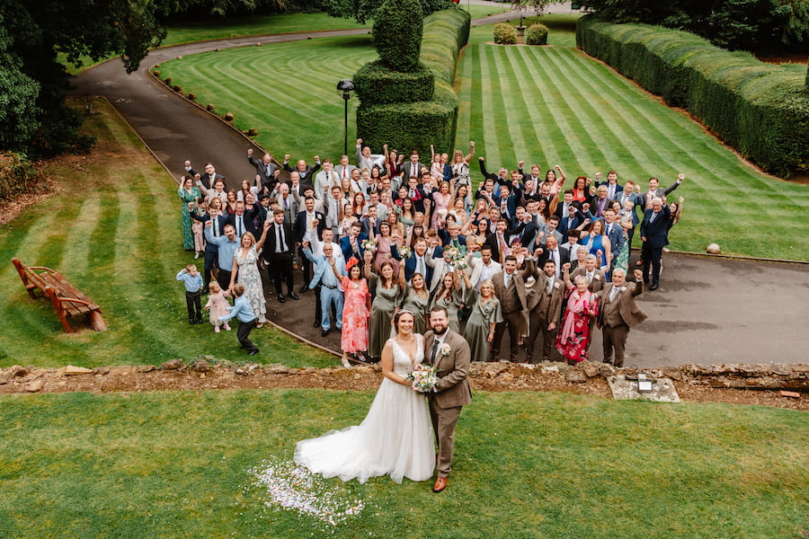 Wedding guests group photo with bride and groom outside Sedgebrook Hall